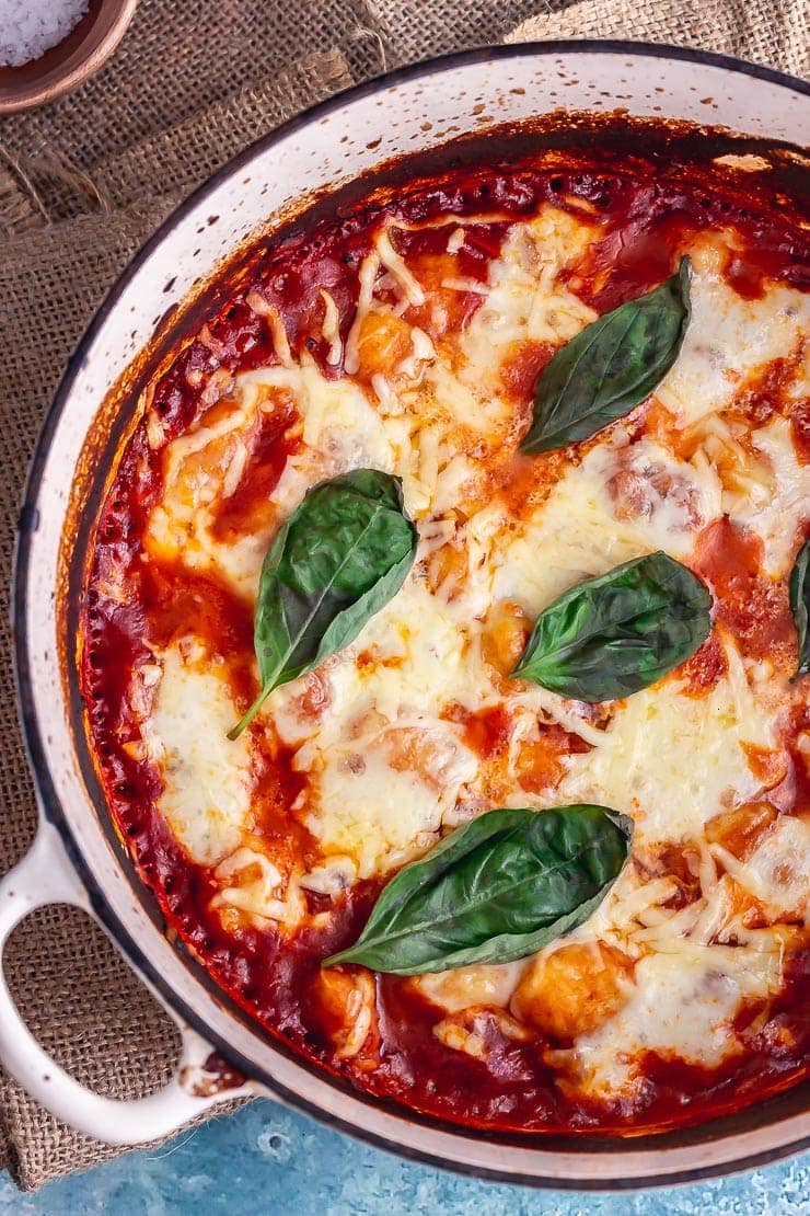 Overhead shot of one pot gnocchi topped with basil leaves on a blue background