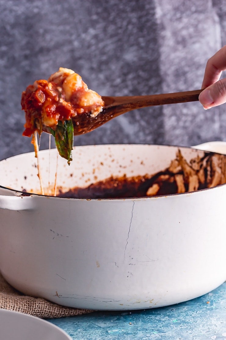 Wooden spoonful of one pot gnocchi with cheese in a white pot