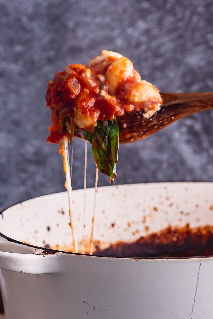 Wooden spoonful of one pot gnocchi bake with cheese on a grey background