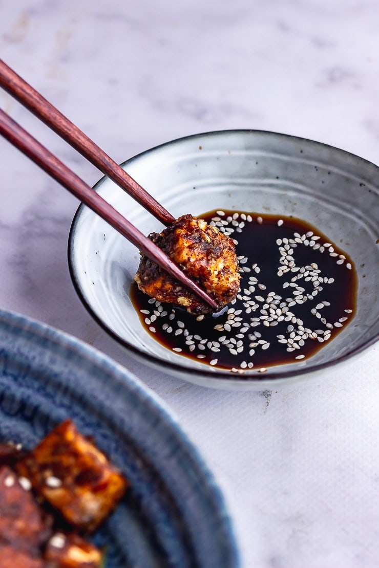 Chopsticks dipping salt and pepper tofu into soy sauce