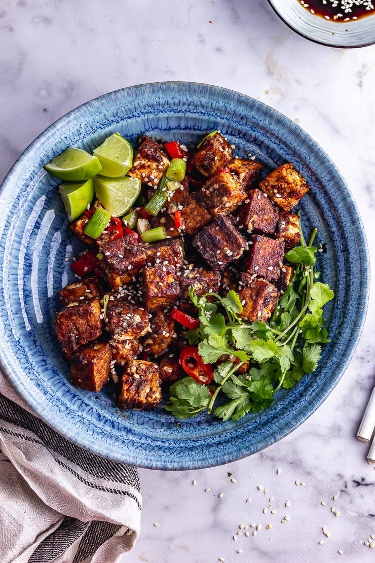 Overhead shot of blue bowl of salt and pepper tofu with lime and coriander on a marble background