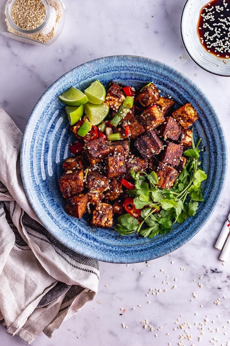 Overhead shot of salt and pepper tofu in a blue bowl with toppings on a marble background