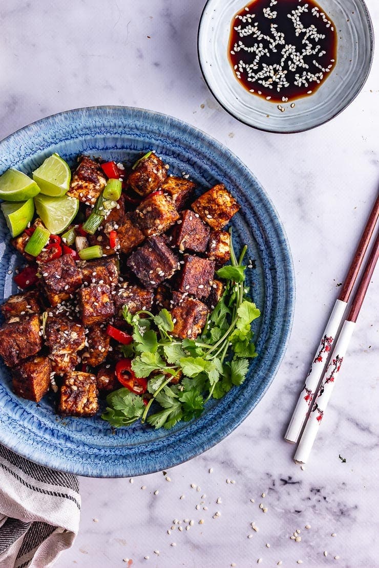 Overhead shot of blue bowl of salt and pepper tofu with soy sauce and chopsticks