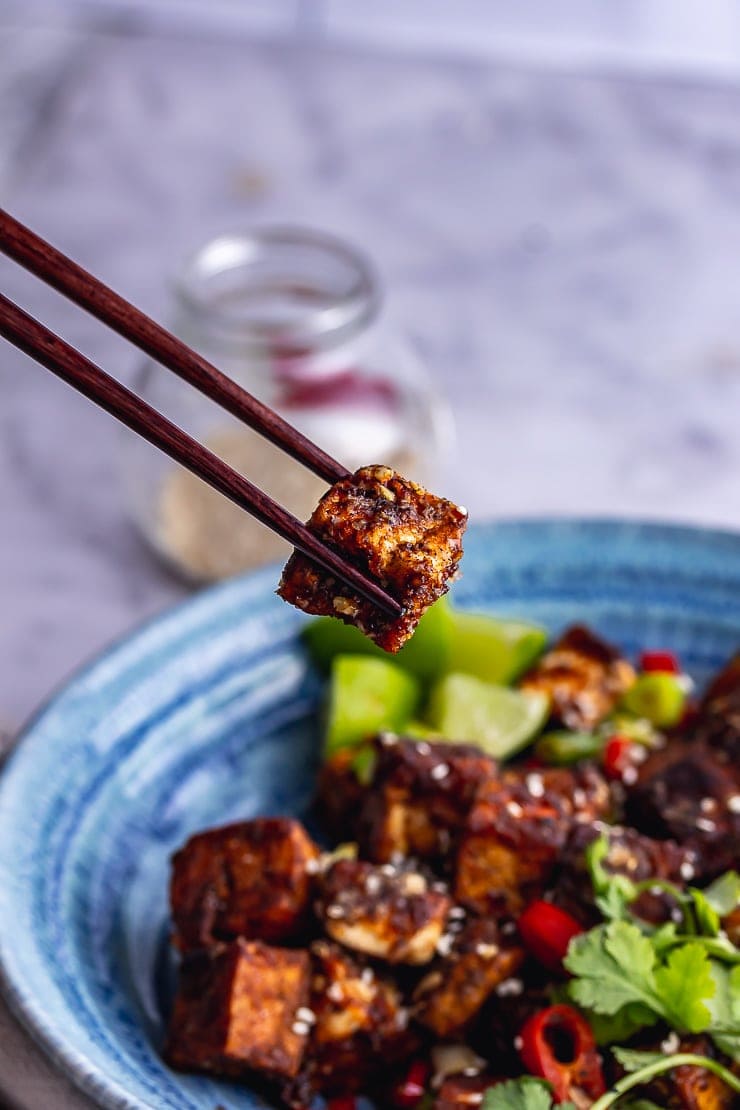 Chopsticks holding a piece of salt and pepper tofu over a blue bowl