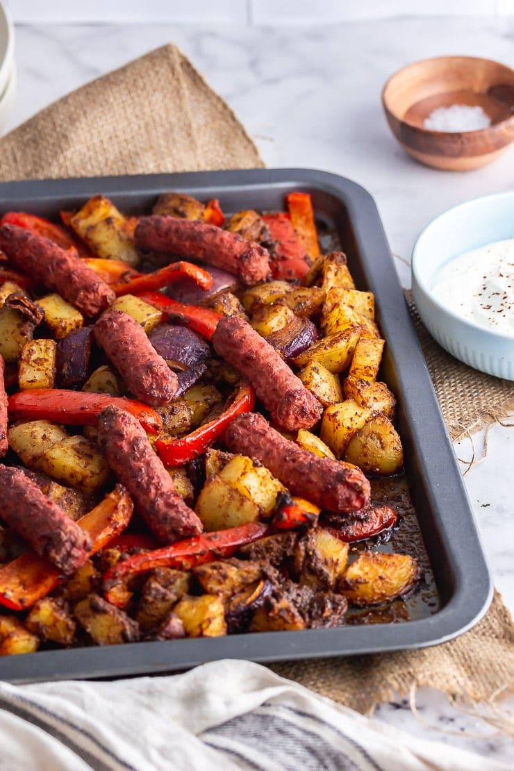 Baking sheet of veggie sausage bake on a marble background with salt and yoghurt
