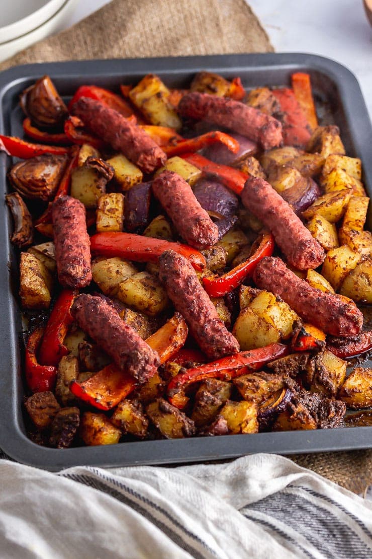 Veggie sausage bake on a grey sheet pan with a hessian cloth