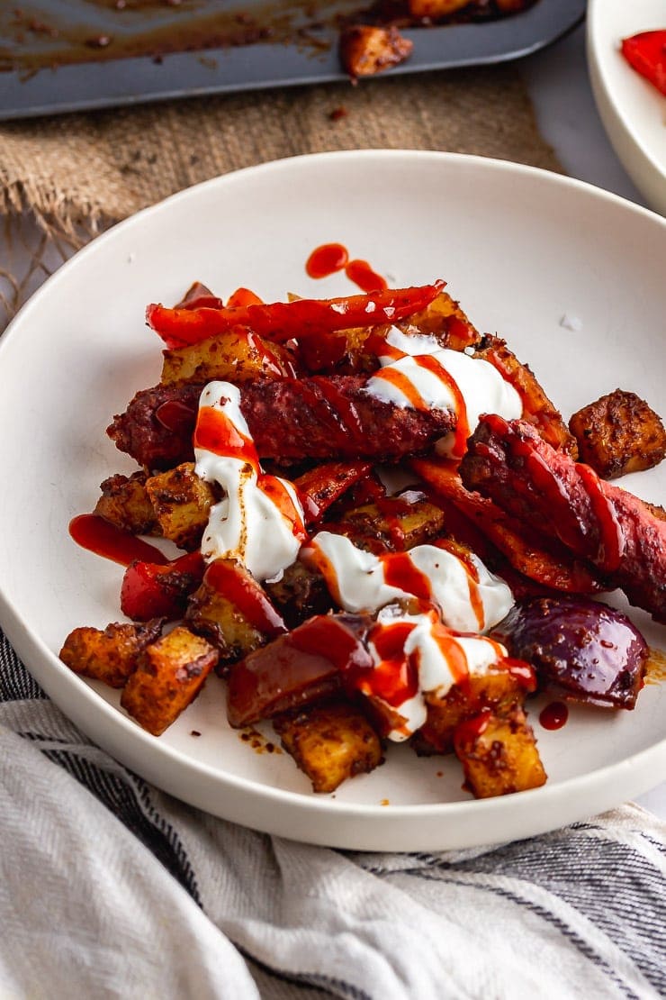 Bowl of veggie sausage bake with yoghurt and chilli sauce on a light cloth