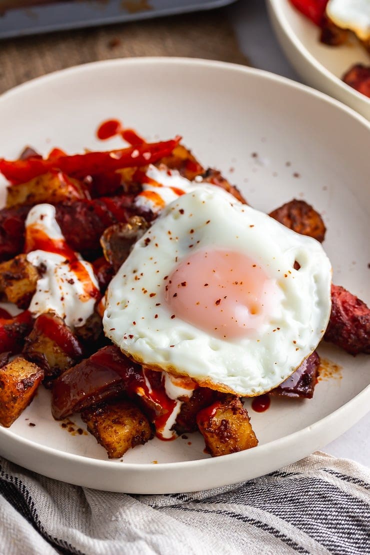 Close up of veggie sausage bake in a white bowl topped with a fried egg