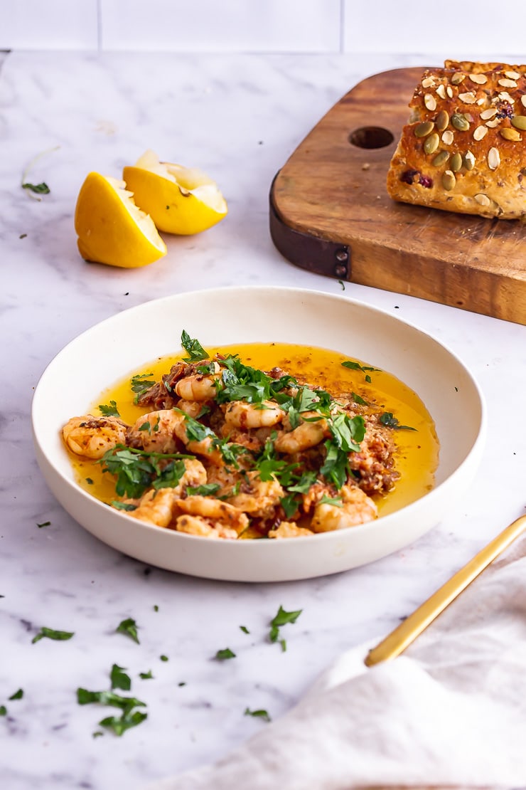 Chilli prawns in a white bowl on a marble background with bread and lemon