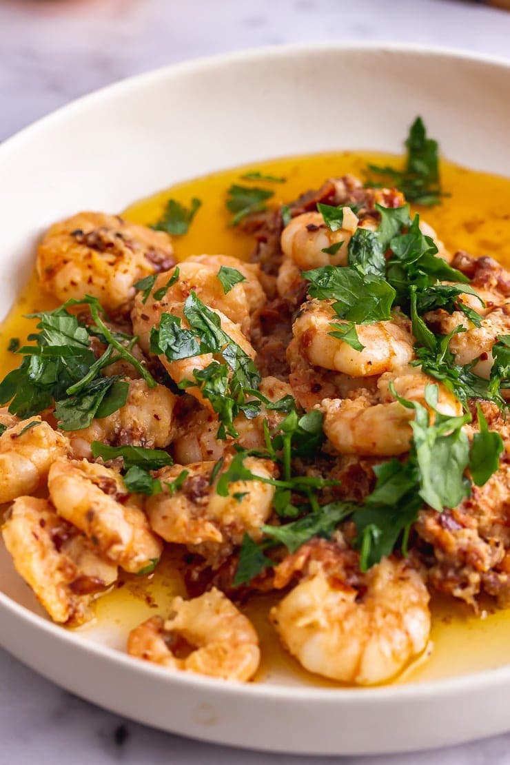 Close up of chilli prawns in a white bowl with parsley