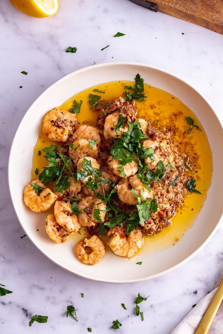 Overhead shot of chilli prawns with tomato butter in a white bowl on a marble background