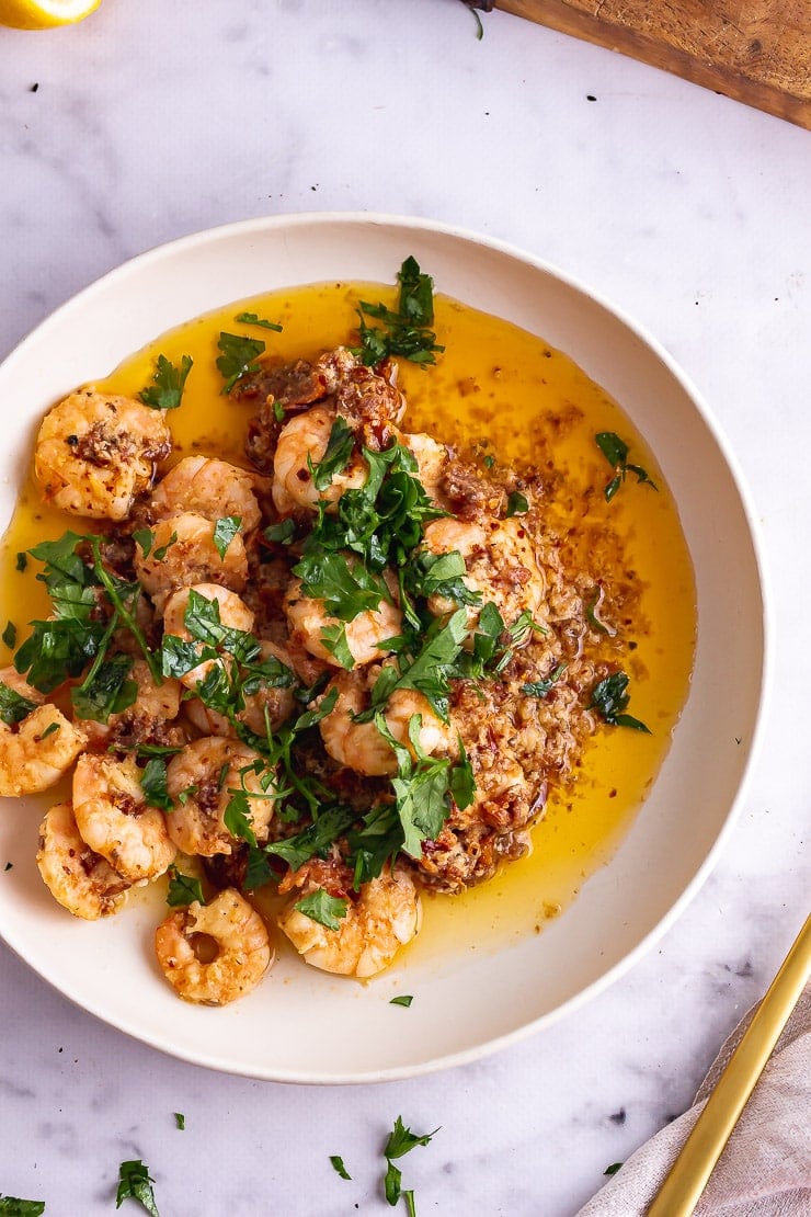 Overhead shot of chilli prawns in a white bowl with parsley 