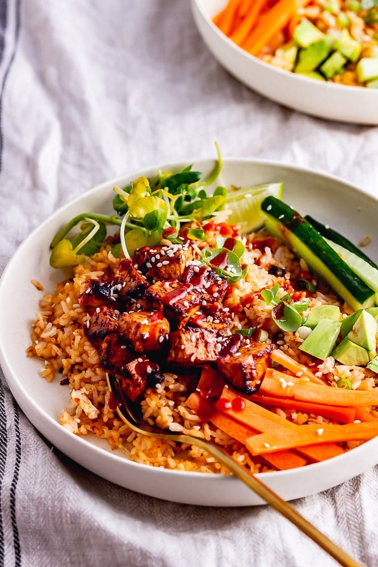 Spicy ruce bowls topped with tofu and vegetables and hot sauce