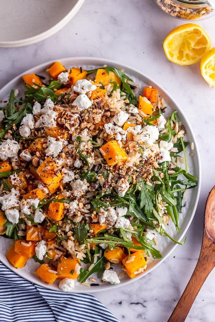 Overhead shot of butternut squash salad with a wooden spoon and lemon