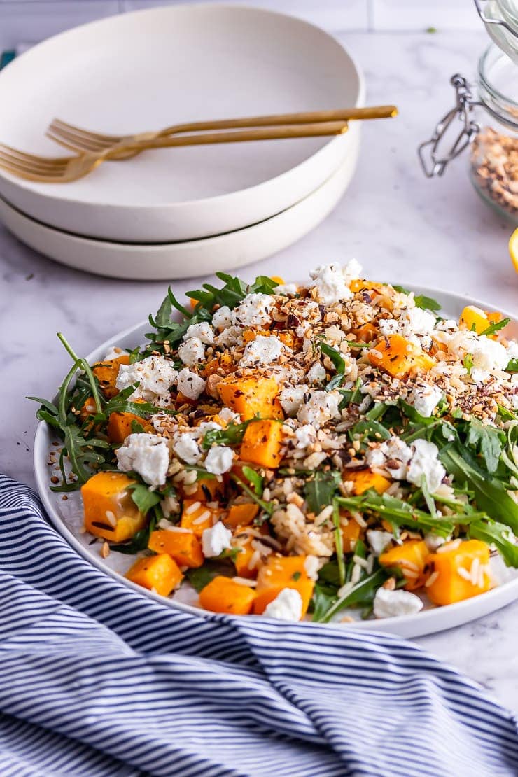 Plate of butternut squash salad on a marble background with a striped cloth