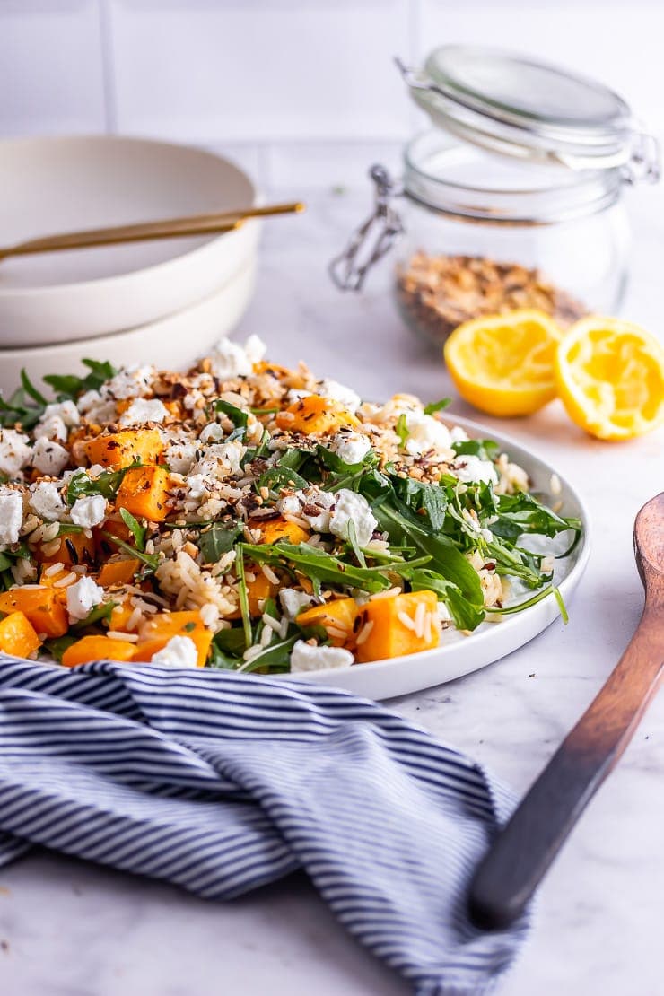 Side on shot of butternut squash salad with a striped cloth and a wooden spoon