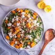 Overhead shot of butternut squash salad with a wooden spoon, bowls and lemon halves