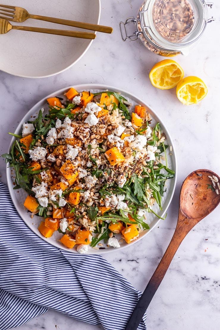 Overhead shot of butternut squash salad with a wooden spoon, bowls and lemon halves