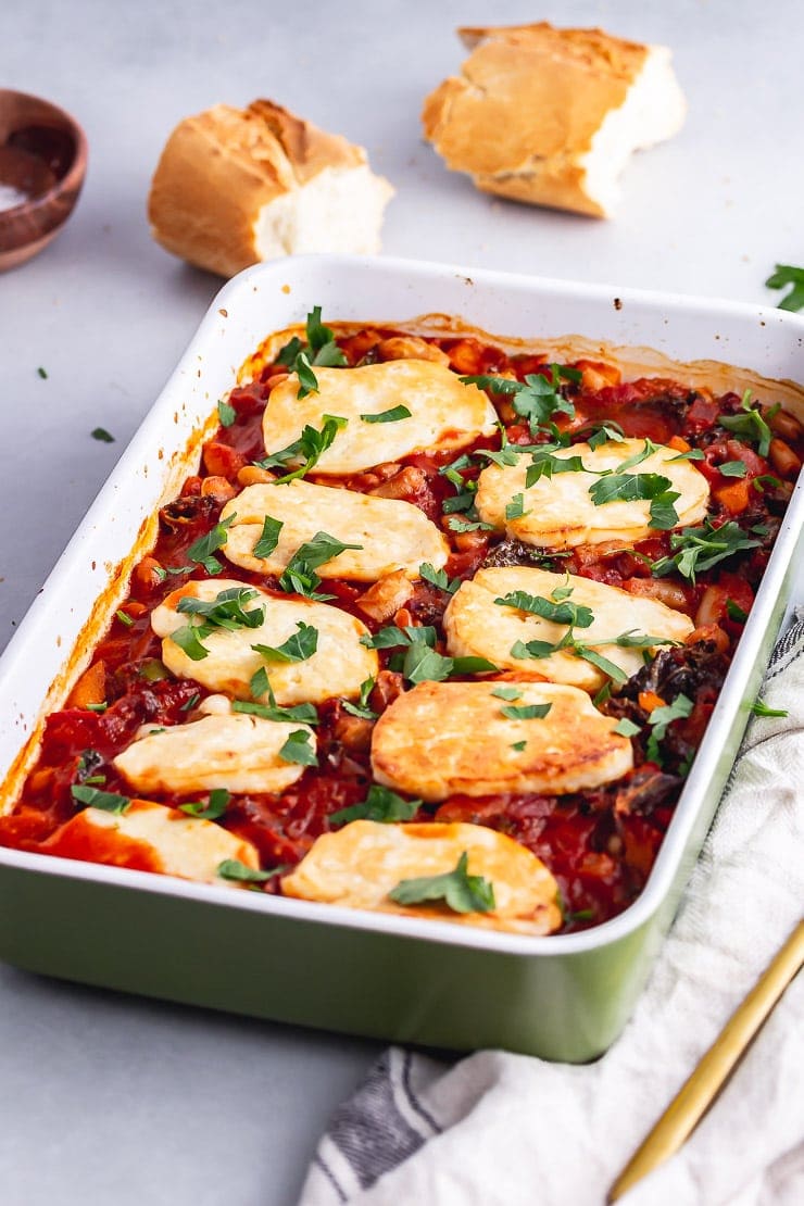 Green baking dish of halloumi, kale & white bean bake with a cloth