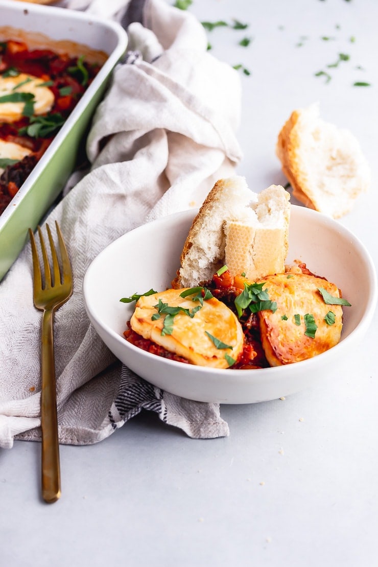 White bowl of halloumi, kale & white bean bake with a gold fork and a cloth