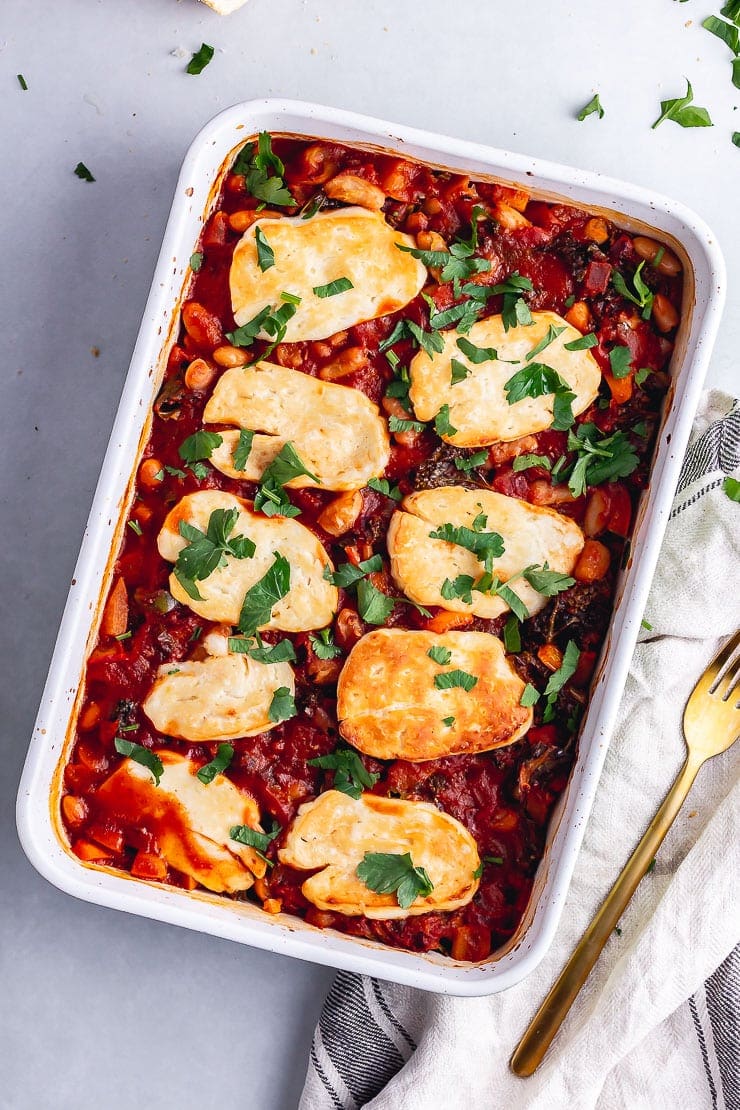 Overhead shot of halloumi bake with white beans on a grey background