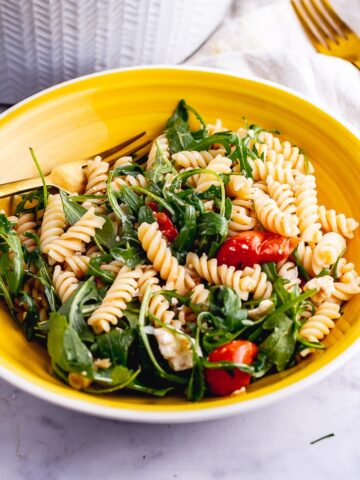 Yellow bowl of roasted tomato pasta salad on a marble background