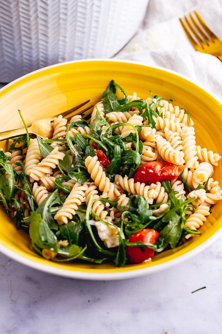 Yellow bowl of roasted tomato pasta salad on a marble background