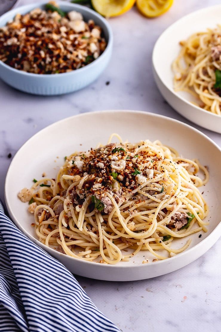 White bowls of tuna pasta with a striped cloth on a marble surface