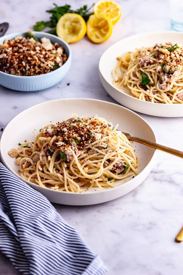 White bowls of tuna pasta with a gold fork on a marble background