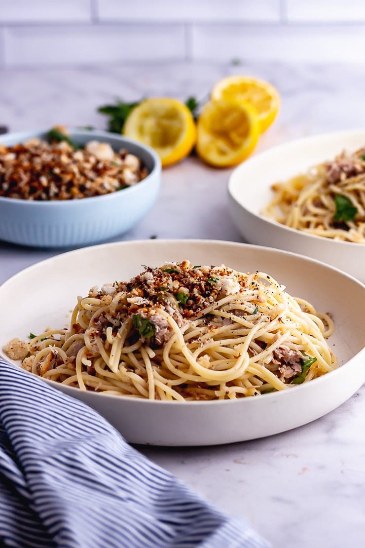 Side on shot of a white bowl of tuna pasta with lemon in the background