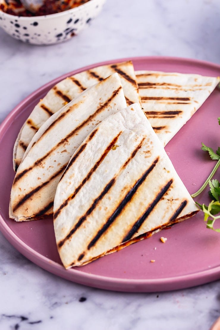Vegetarian quesadilla quarters on a pink plate with coriander