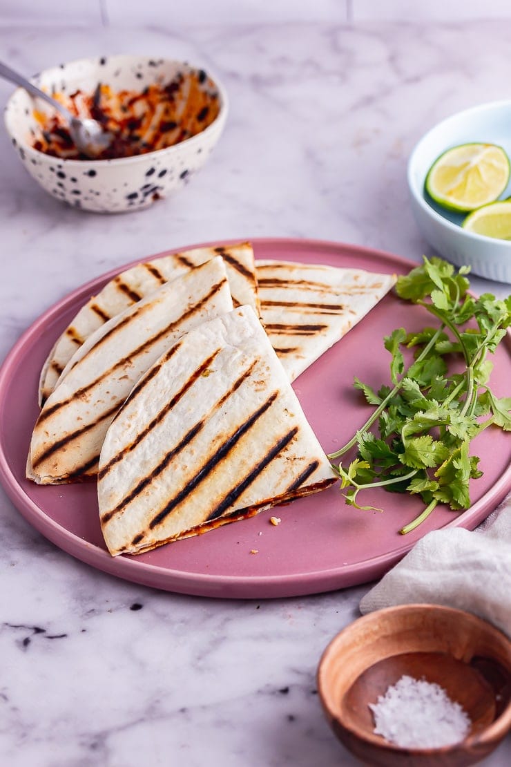 Vegetarian quesadilla quarters on a pink plate over a marble background