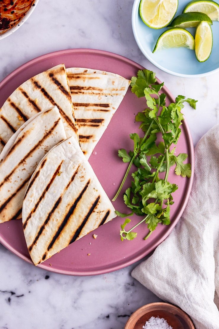 Overhead shot of a vegetarian quesadilla on a pink plate with lime and salt