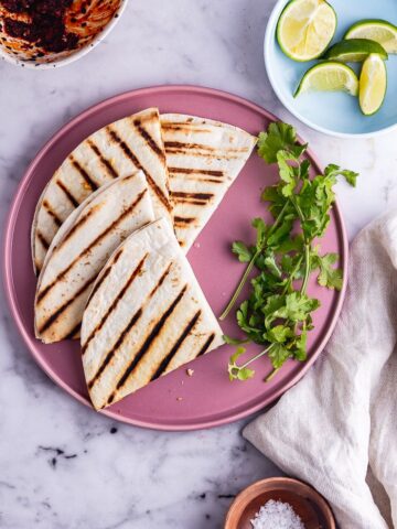 Overhead shot of vegetarian quesadillas on a pink plate with limes