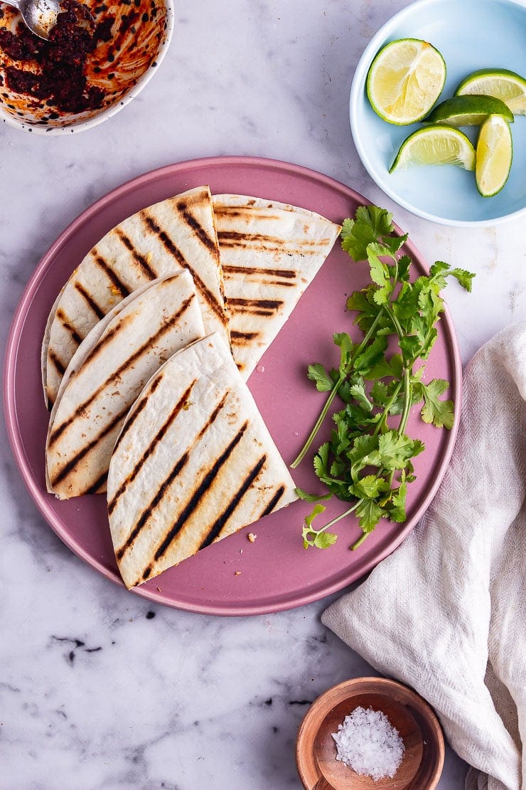 Overhead shot of vegetarian quesadillas on a pink plate with limes