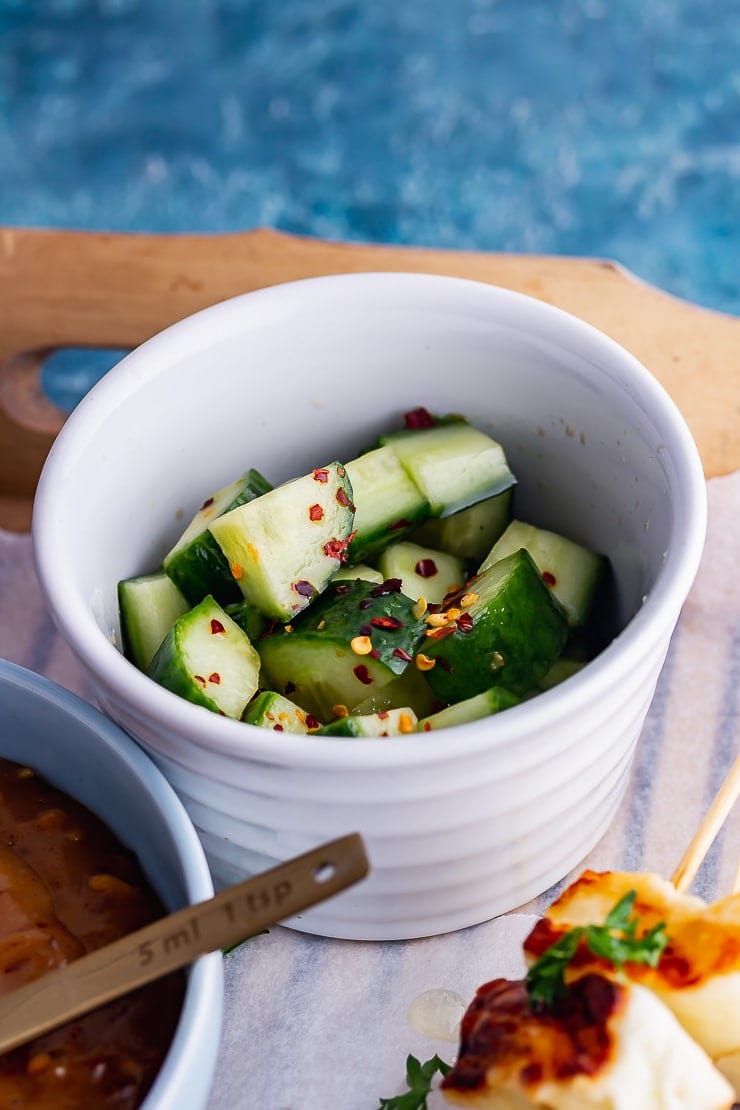 White bowl of cucumber salad on a wooden tray
