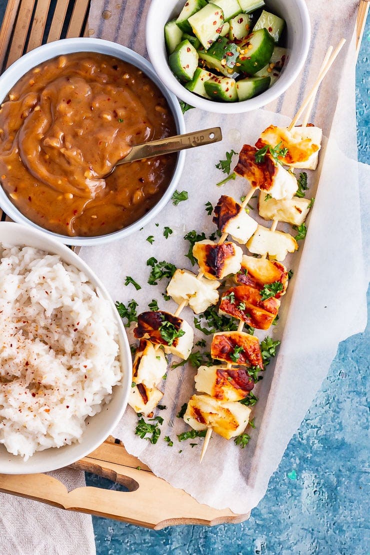 Overhead shot of halloumi skewers with satay sauce and rice on a wooden tray
