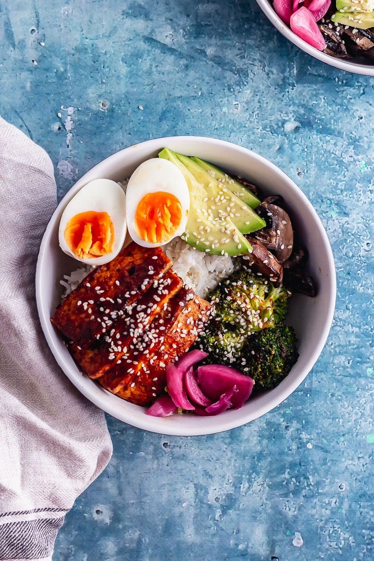 Overhead shot of Korean baked tofu rice bowl with a cloth on a blue surface