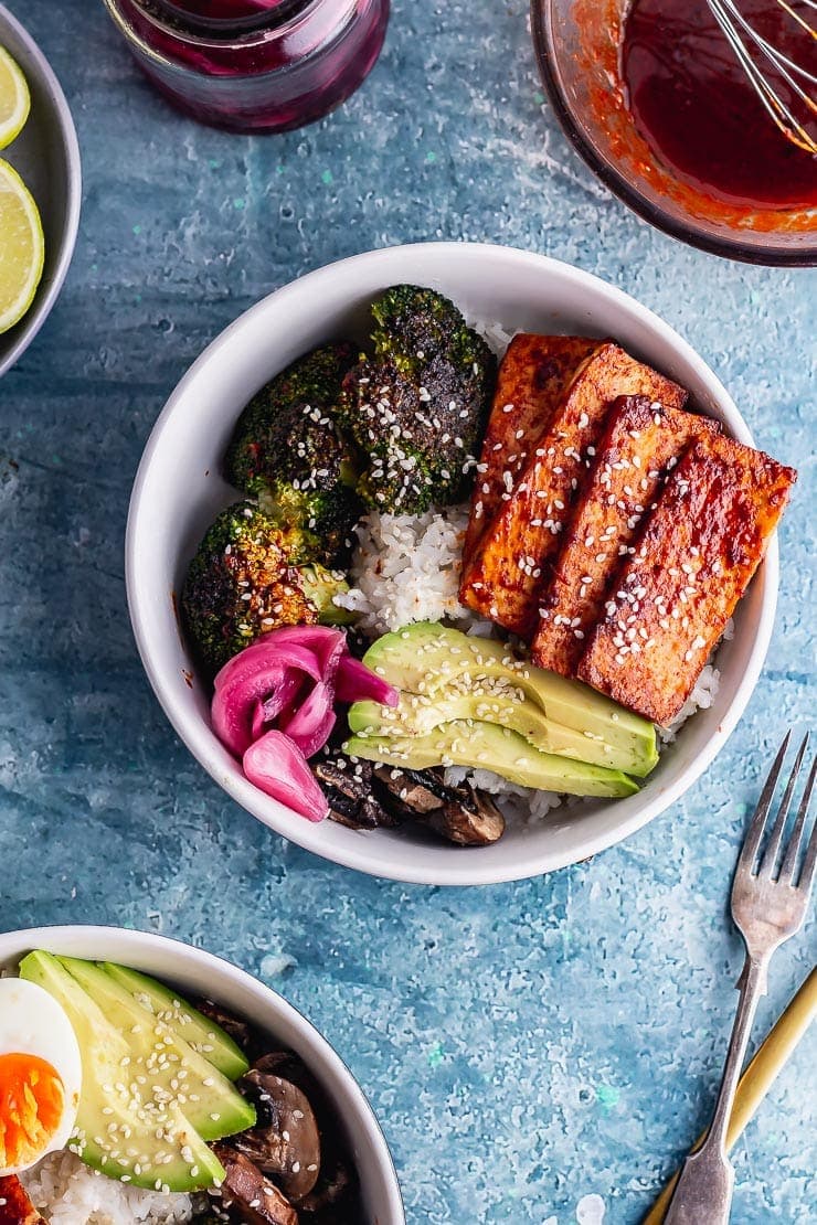 Overhead shot of tofu bowl on a blue background with a fork and sauce