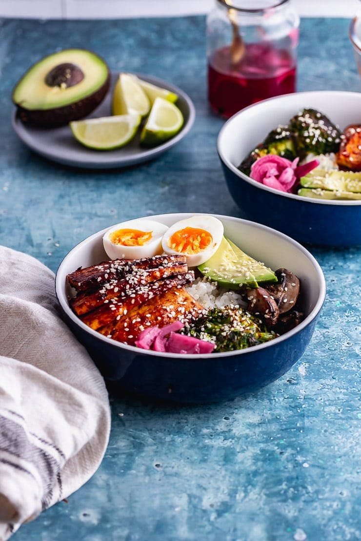 Side on shot of two bowls of Korean baked tofu rice bowls on a blue background