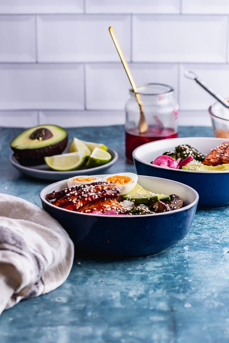Side on shot of Korean baked tofu rice bowls on a blue surface with avocado and lime