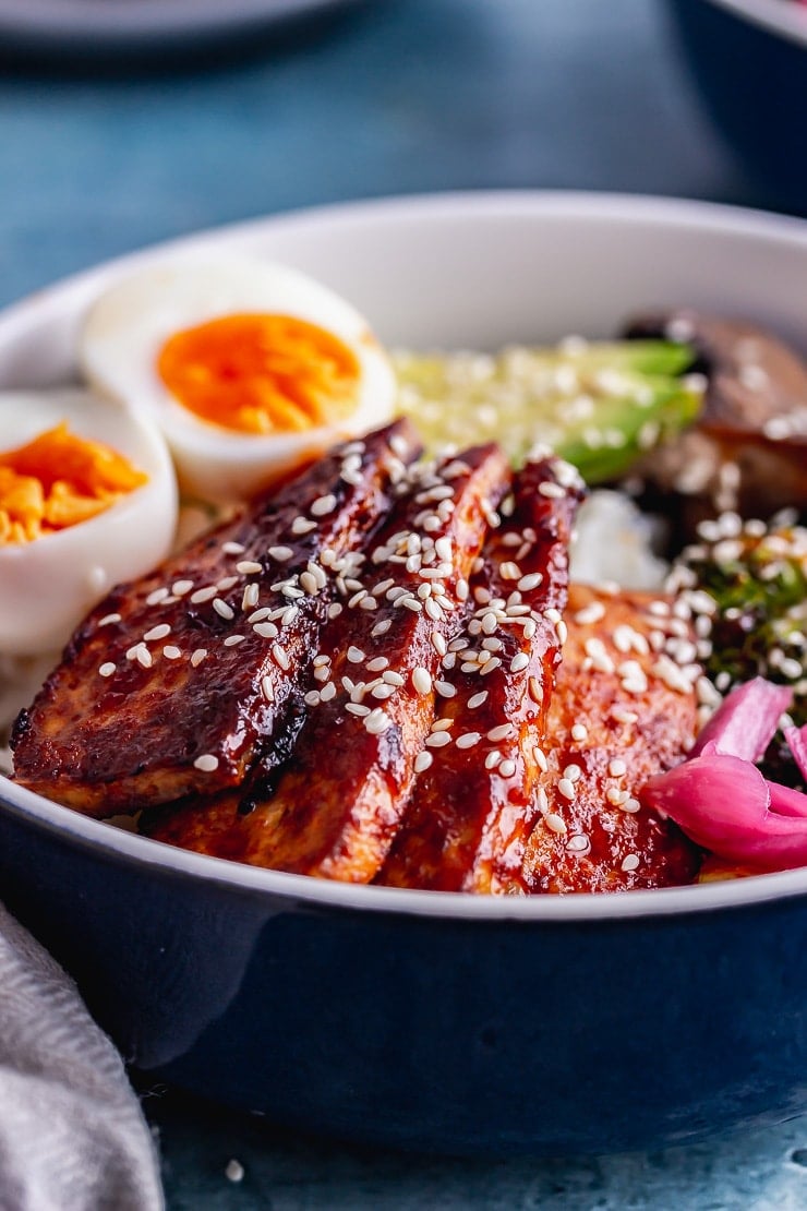 Close up of glazed tofu on rice in a blue bowl