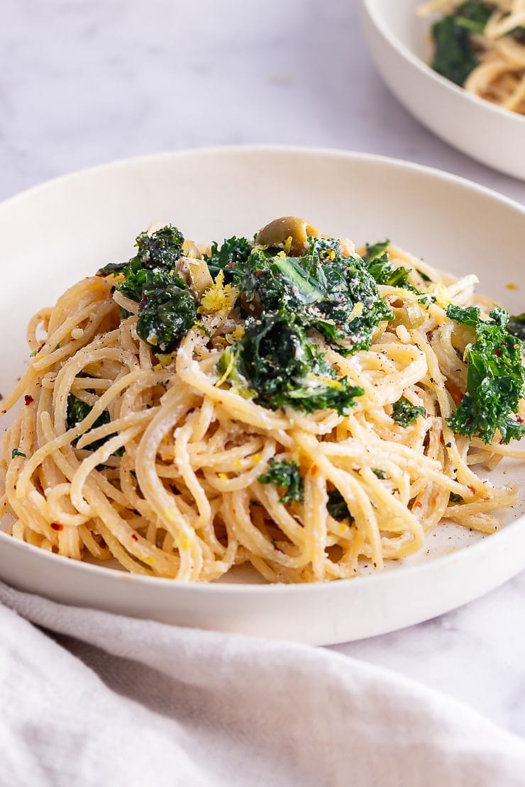 White bowl of roasted garlic spaghetti with a cloth on a marble background