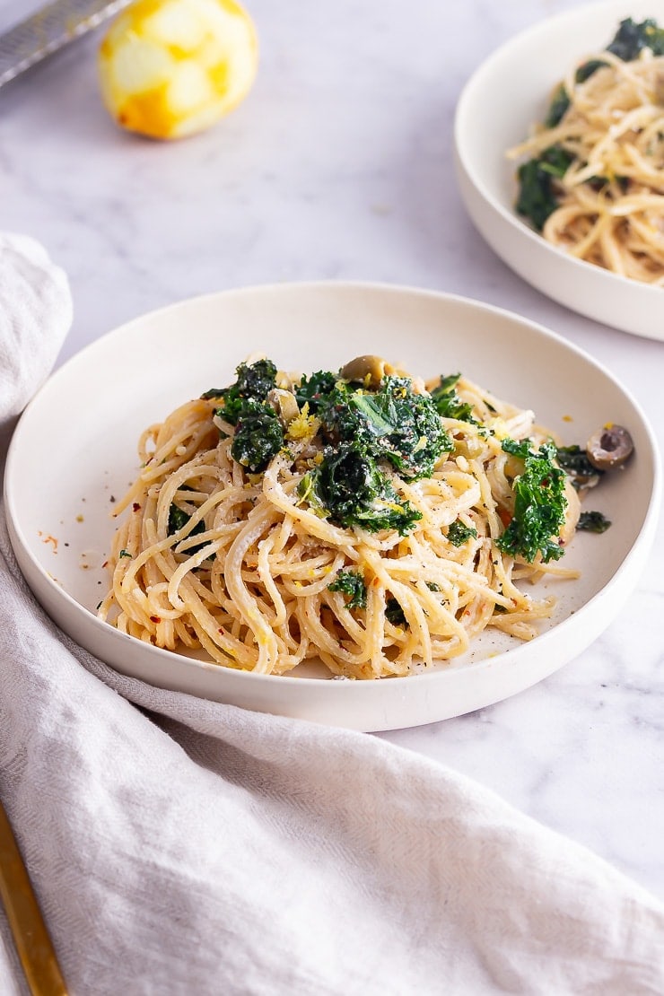 White bowl of roasted garlic spaghetti with kale and a lemon