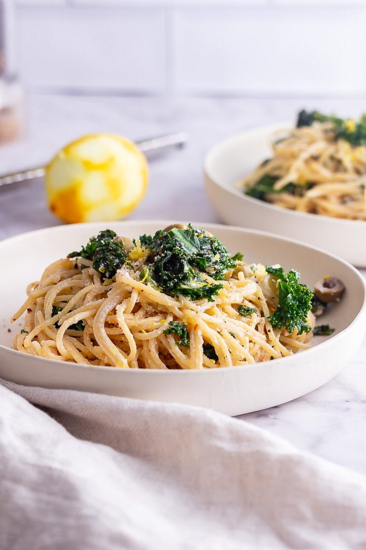 Side on shot of roasted garlic spaghetti with kale in a white bowl on a marble surface