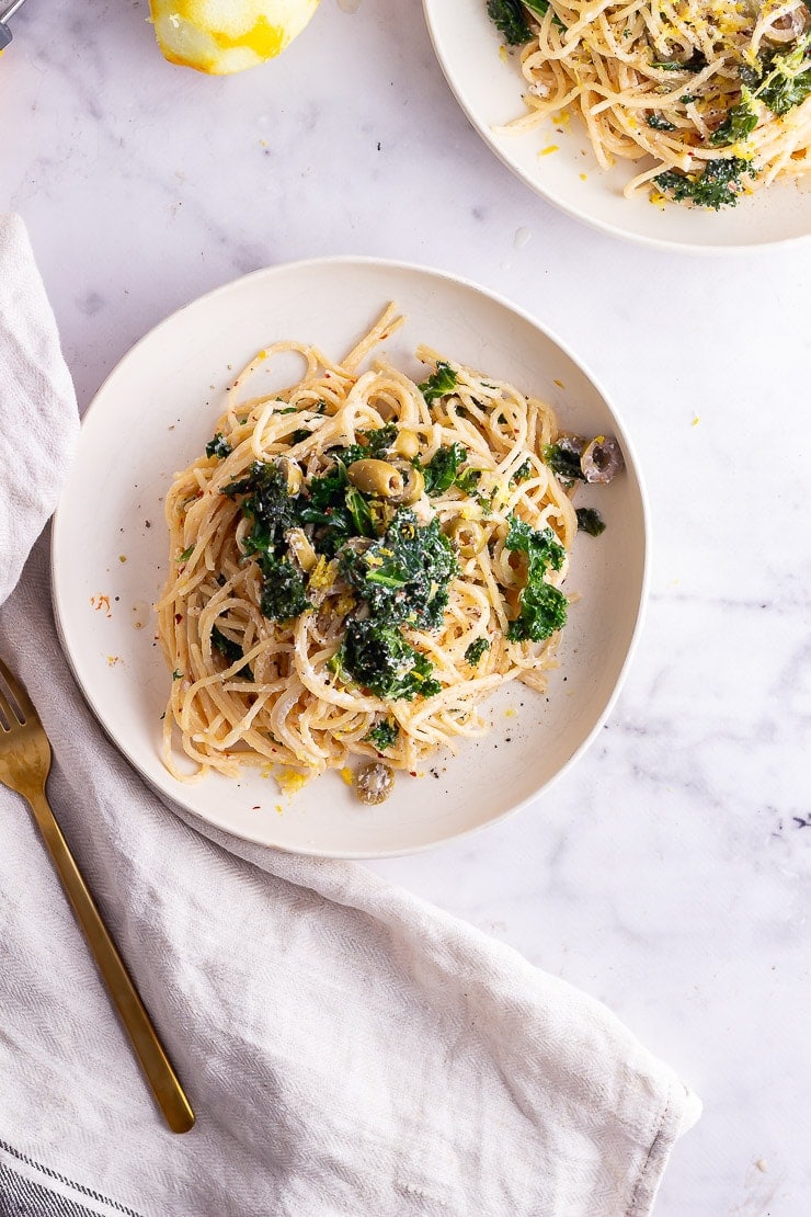 Overhead shot of white bowls of garlic spaghetti with kale on a marble surface