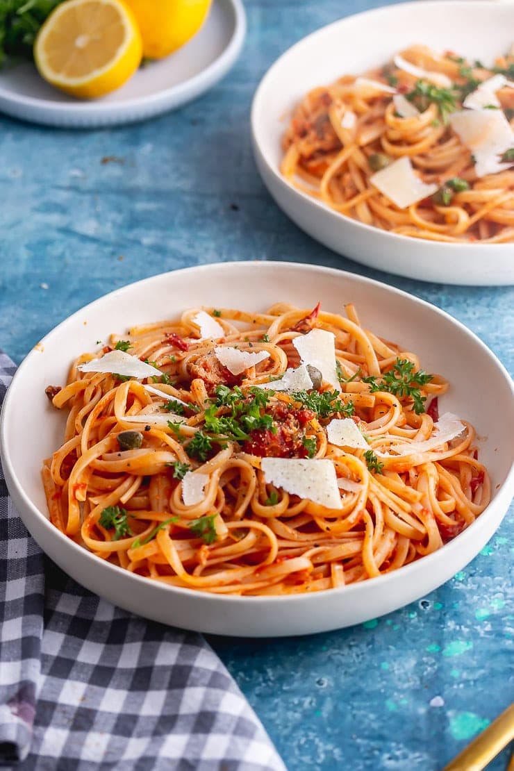 White bowl of spicy salmon pasta on a blue background with a checked cloth