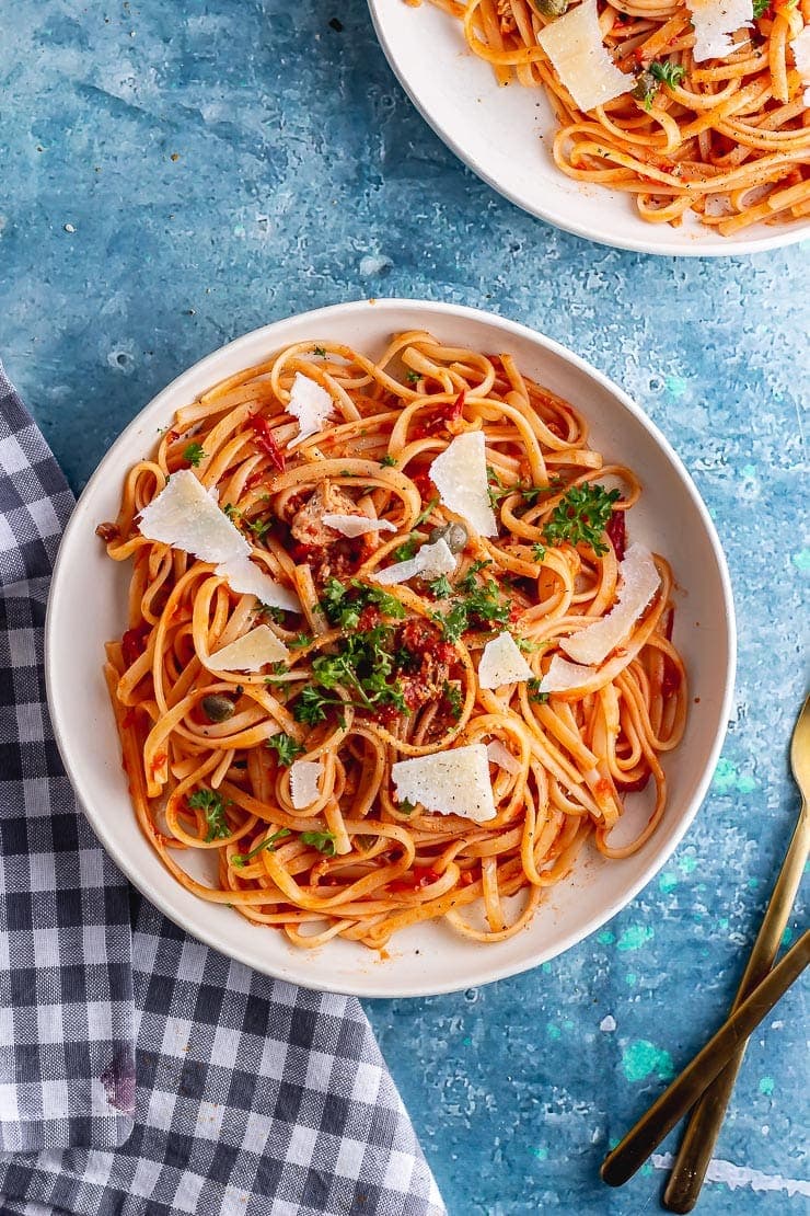 Overhead shot of salmon pasta with parmesan and parsley on a blue background with a checked cloth