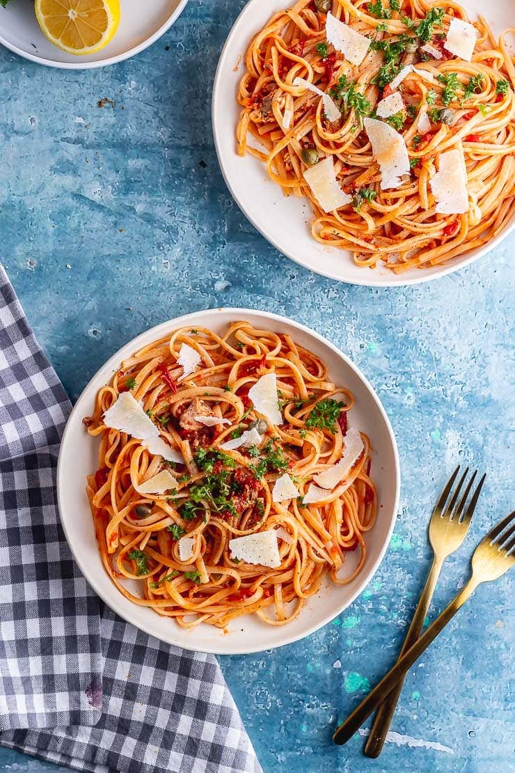 Overhead shot of two bowls of spicy salmon linguine with gold forks and lemon halves