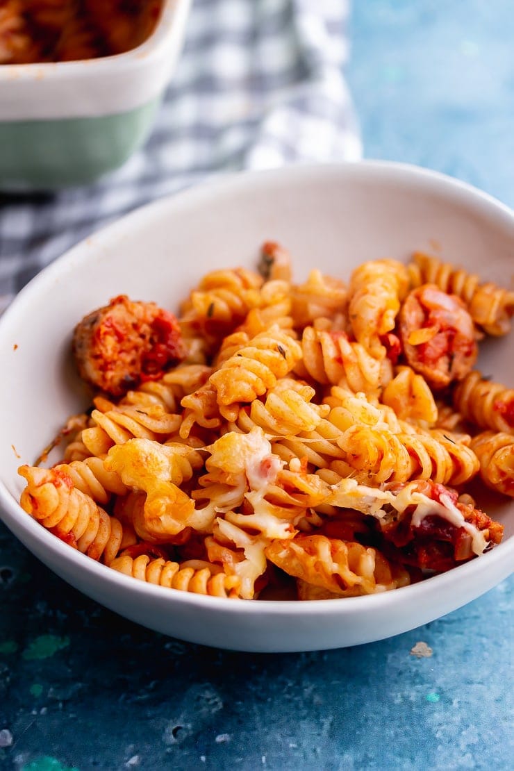 White bowl of a portion of veggie sausage pasta bake on a blue background